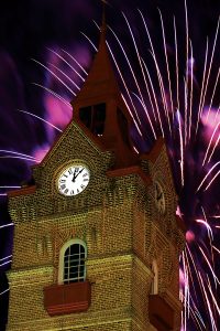 Fireworks explode over a purple sky behind the newberry opera house clock tower