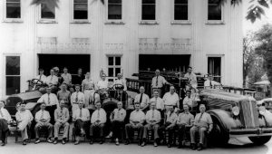 An historic photo of men from the city of Newberry sitting in front of three old firetrucks